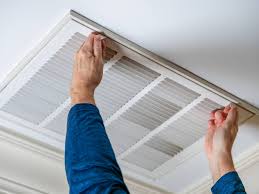 Person removing or installing a rectangular air vent cover on a ceiling.